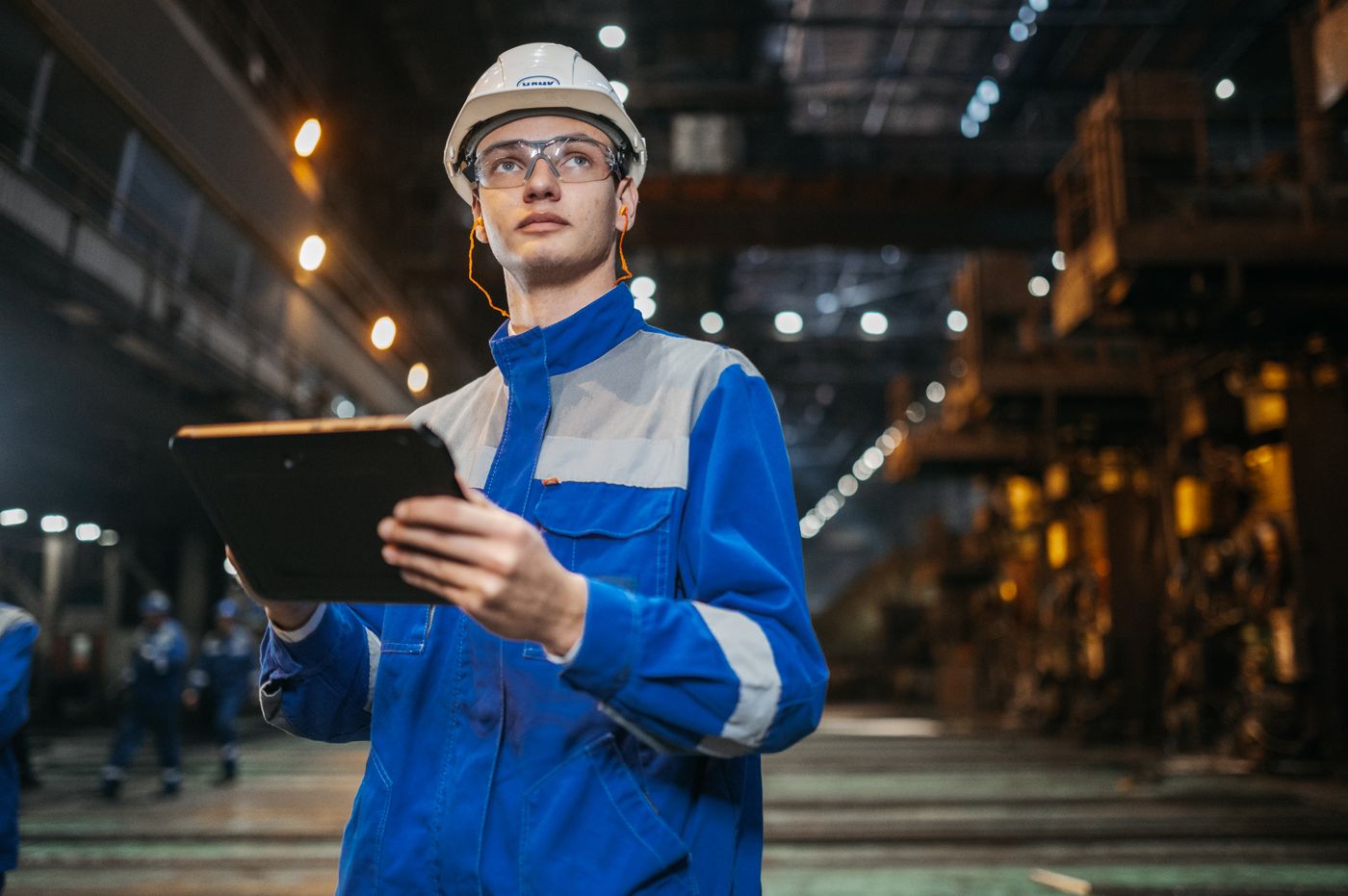 An engineer reviewing production data on a tablet in an industrial facility.